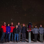 Una imagen nocturna con algunos miembros de la reunión de personalidades en CASLEO, junto a un telescopio. Al fondo el cielo estrellado, en el cual destaca Marte y los cúmulos de estrellas Pléyades (7 cabritos) y las Hyades.