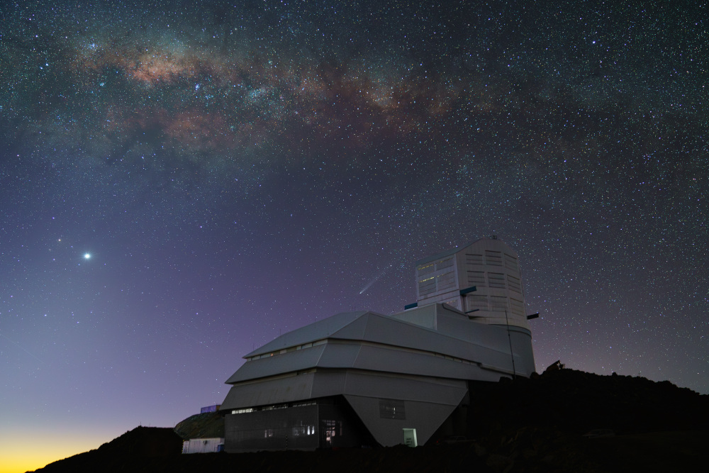 El cielo nocturno deslumbra sobre el Observatorio Rubin en esta foto de octubre de 2024. La Vía Láctea se extiende sobre nosotros en la luz menguante del atardecer. Venus brilla intensamente a la izquierda, mientras que el cometa C/2023 A3 (Tsuchinshan-ATLAS) aparece justo encima del observatorio en el centro.